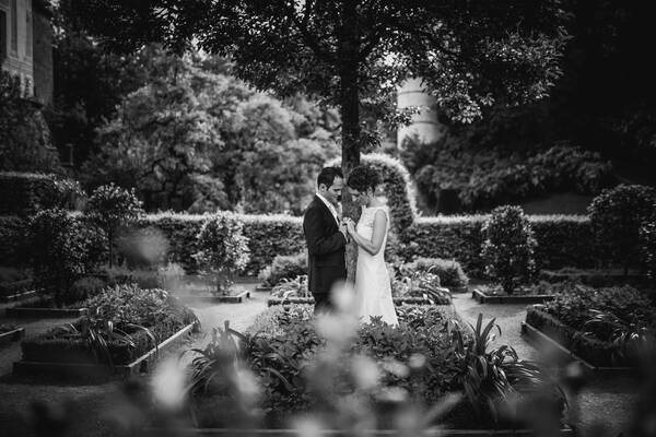 Ein Brautpaar steht sich in einem eleganten Garten gegenüber und hält sich an den Händen. Schwarz-Weiß..