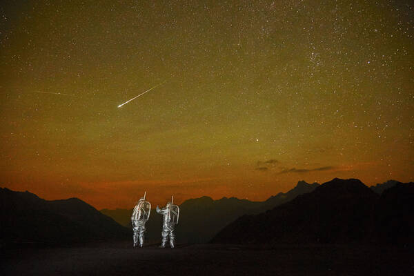 zwei Astronauten stehen in einer von Berggipfeln eingerahmten Landschaft. Am gold-orangen Himmel siieht man Sterne und Sternschnuppen.
