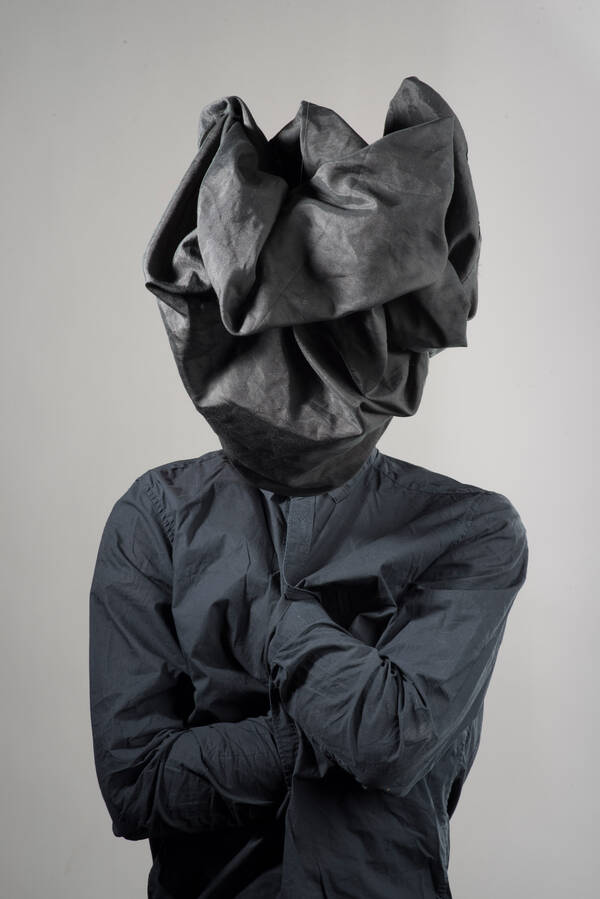 Mann  mit verschränkten Armen, die Hände ins Hemd gesteckt und mit einem Sack über den Kopf.