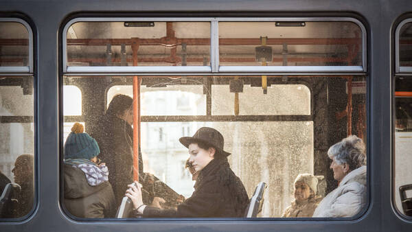 Blick durch eine regennasse Scheibe in ein öffentliches Verkehrsmittel, in dem Menschen sitzen.
