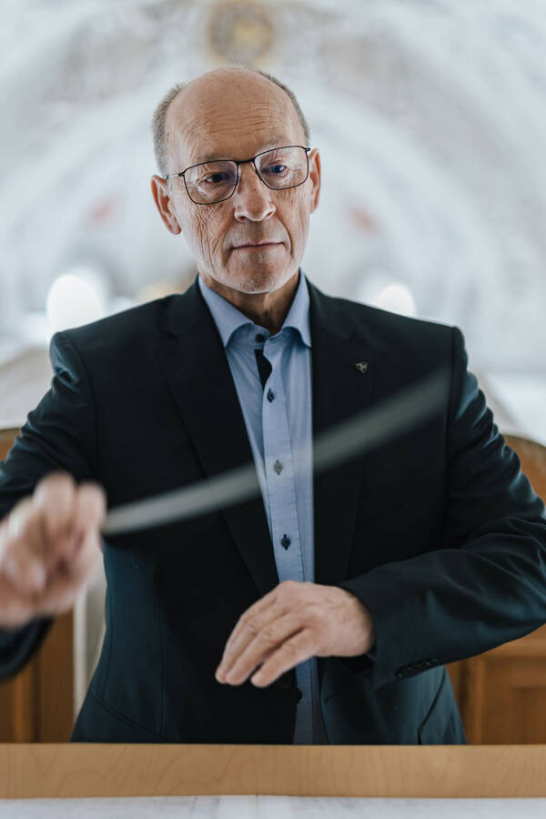 Ein älterer Mann steht dirigierend auf der Empore einer barocken Kirche.