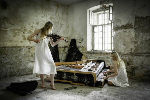 Zwei Frauen in einem verfallenden Haus. Eine spielt Geige, die andere sitzt vor dem eingestürzten Klavier.