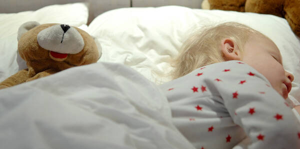 Baby und Teddybär im Bett.