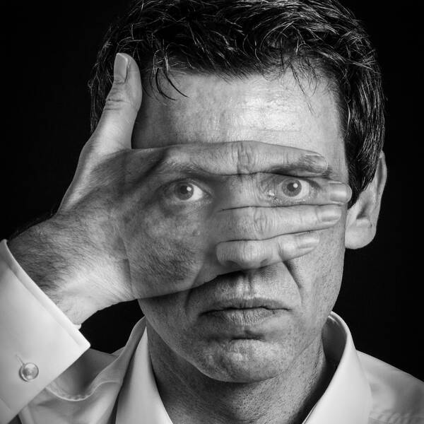 Ein Mann hält sich die rechte Hand vor die Augen, die aber durch die Hand durchscheinen. Schwarz-Weiß