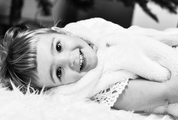 Ein Kind liegt auf einem weißen Fell und lacht in die Kamera. Schwarz-Weiß