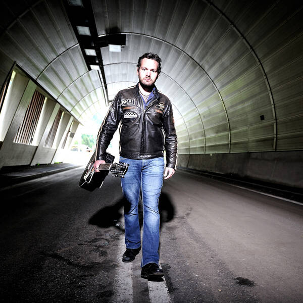 Ein Mann mit Gitarre geht auf der doppelten Sperrlinie in einem Tunnel.