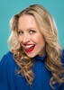 Portrait der Schauspielerin Nina Proll, die sich mit der Zunge über die Zähne schleckt.