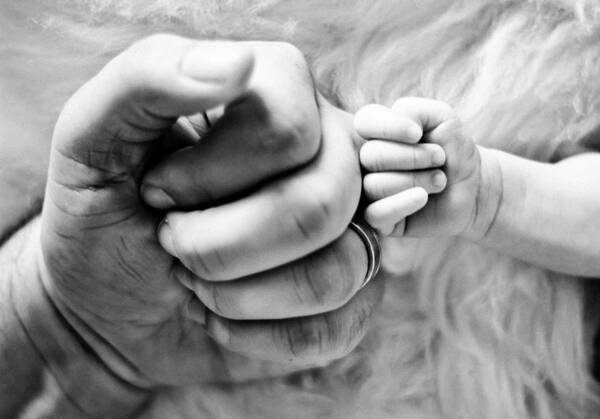 Die Faust eines Erwachsenen berührt die Faust eines Babies. Schwarz-Weiß.
