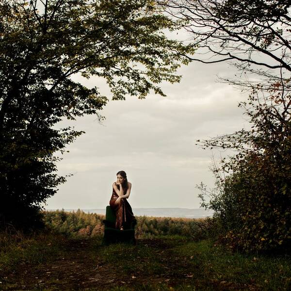 Die italienische Pianistin Saskia Giorgini sitzt auf der Lehne eines alten Fauteuils der mitten in der Landschaft steht.