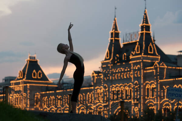 Eine Frau in tänzerischer Pose im Abendlich vor dem beleuchteten Kaufhaus GUM in Moskau.