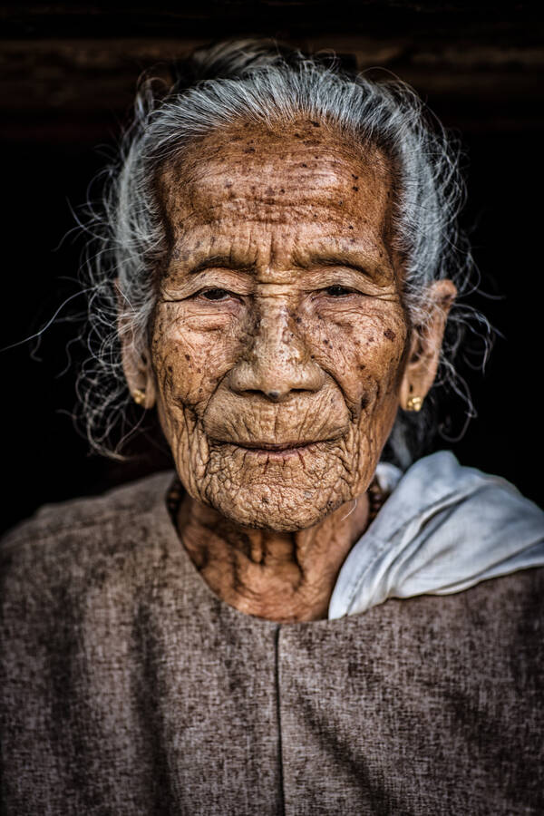Portrait einer alten, weißhaarigen Frau in grobem Leinengewand.