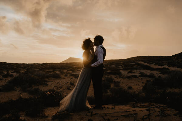 Ein Brautpaar küsst sich in der Untergehenden Sonne in karger, Gebirgslandschaft.