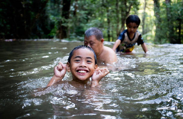 Asiatische Kinder und ein älterer beleibter Mann im Wasser in einem Wald.